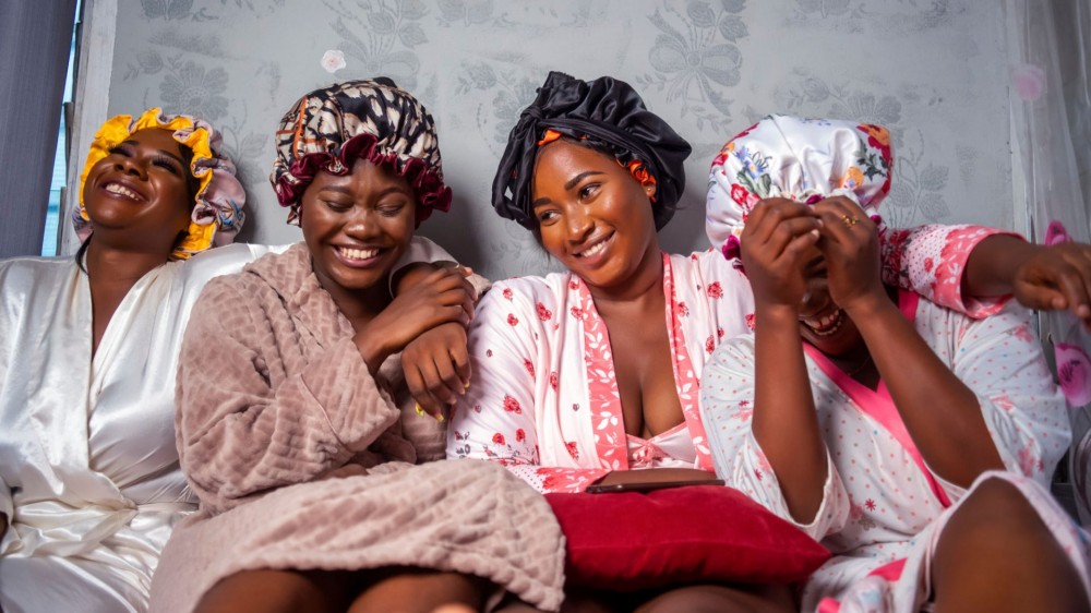 Four beautiful African American girlfriends wearing hair bonnets and robes.