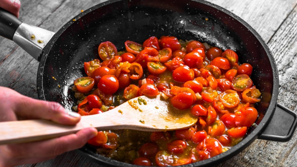 Cooking cherry tomatoes in a large skillet.