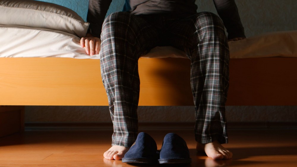 Man sits on a bed in the night at home.