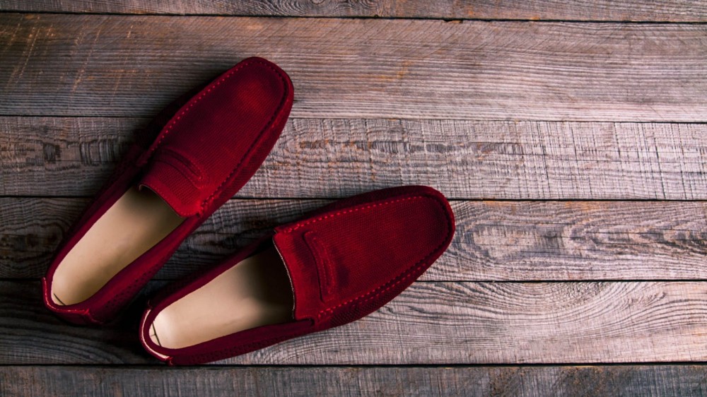 A pair of men's burgundy loafers sit on a wooden surface.