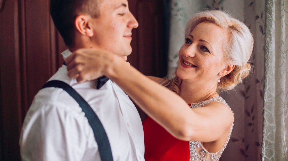 Mother is helping with a bow-tie to her son before wedding ceremony.