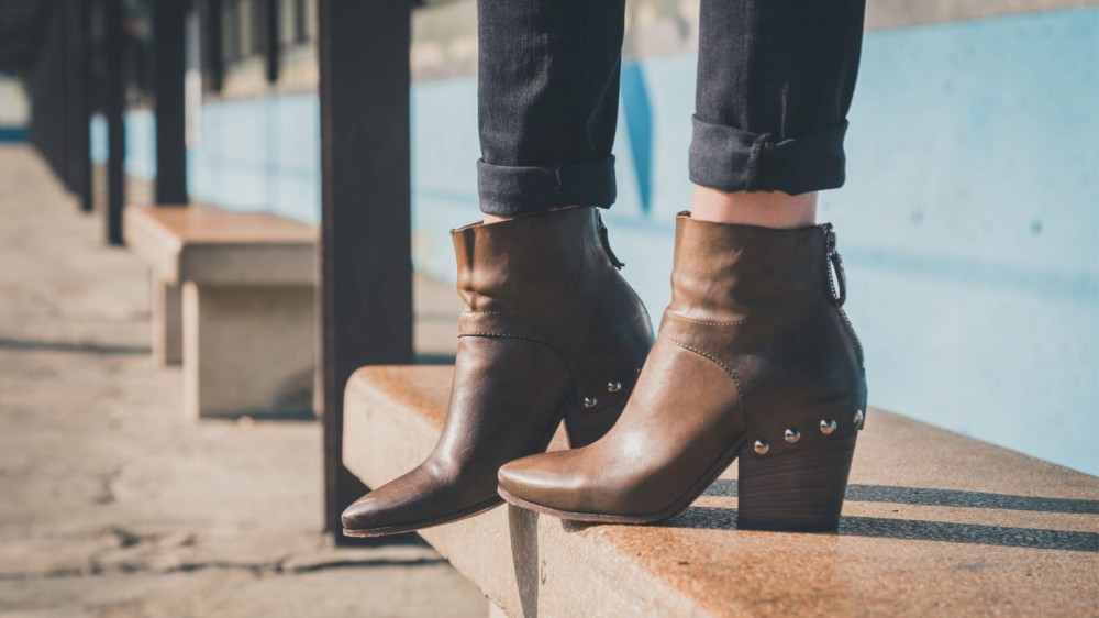 A close-up of a woman wearing brown ankle boots while standing on a step.