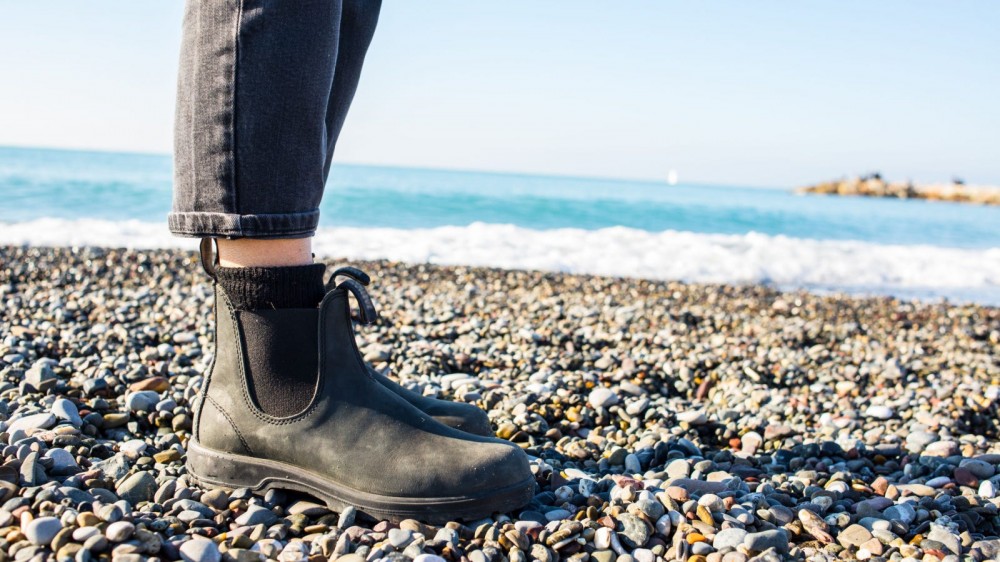 A person standing on a rocky beach wearing Chelsea boots.