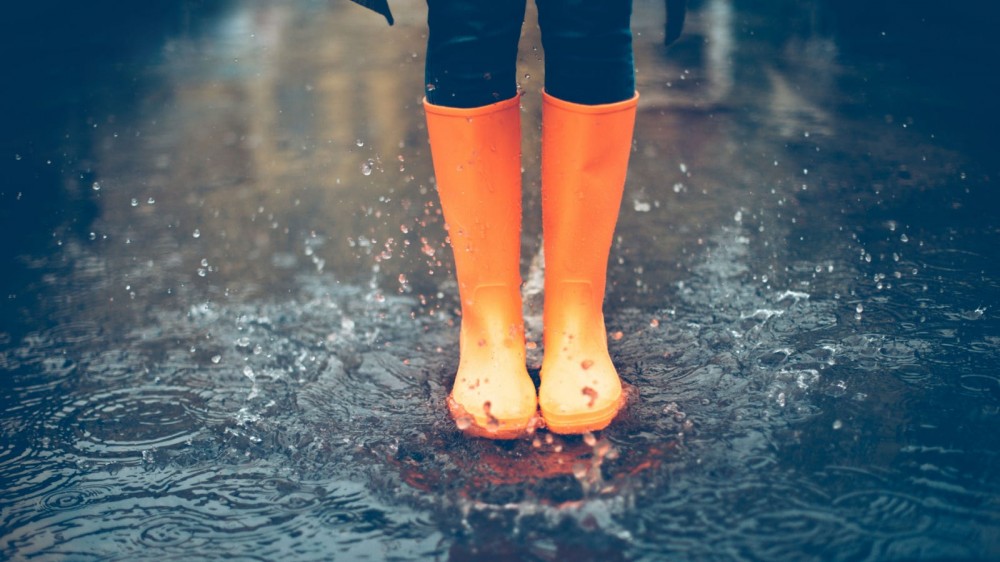 A person wearing orange rain boots jumping in a puddle.