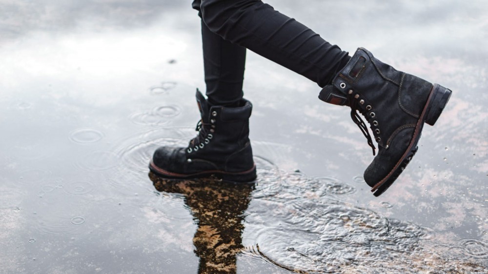 A person wearing black combat boots walking through the rain.