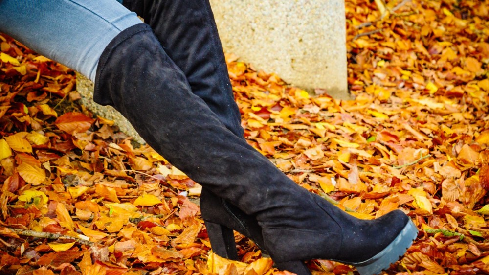 A person wearing black over-the-knee boots in the fall.