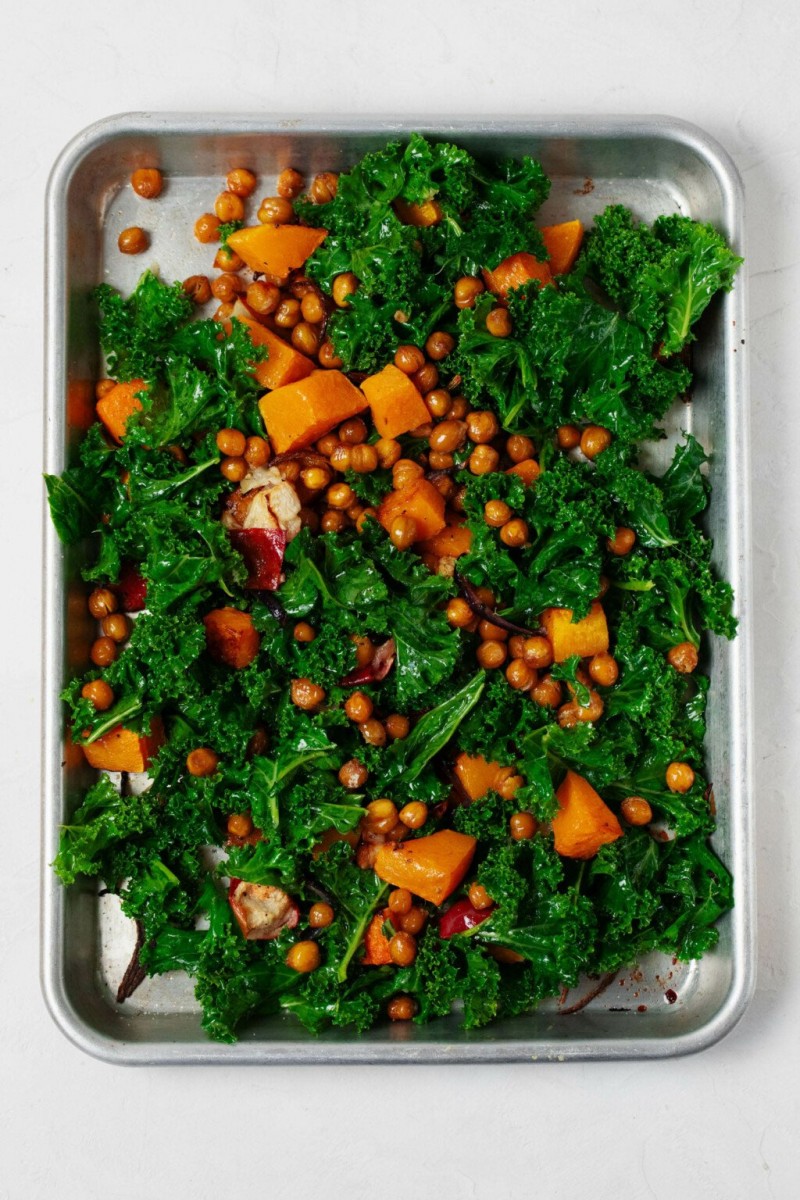 An overhead image of a metal sheet pan, which is covered in a festive kale saiad with roasted butternut squash and chickpeas.