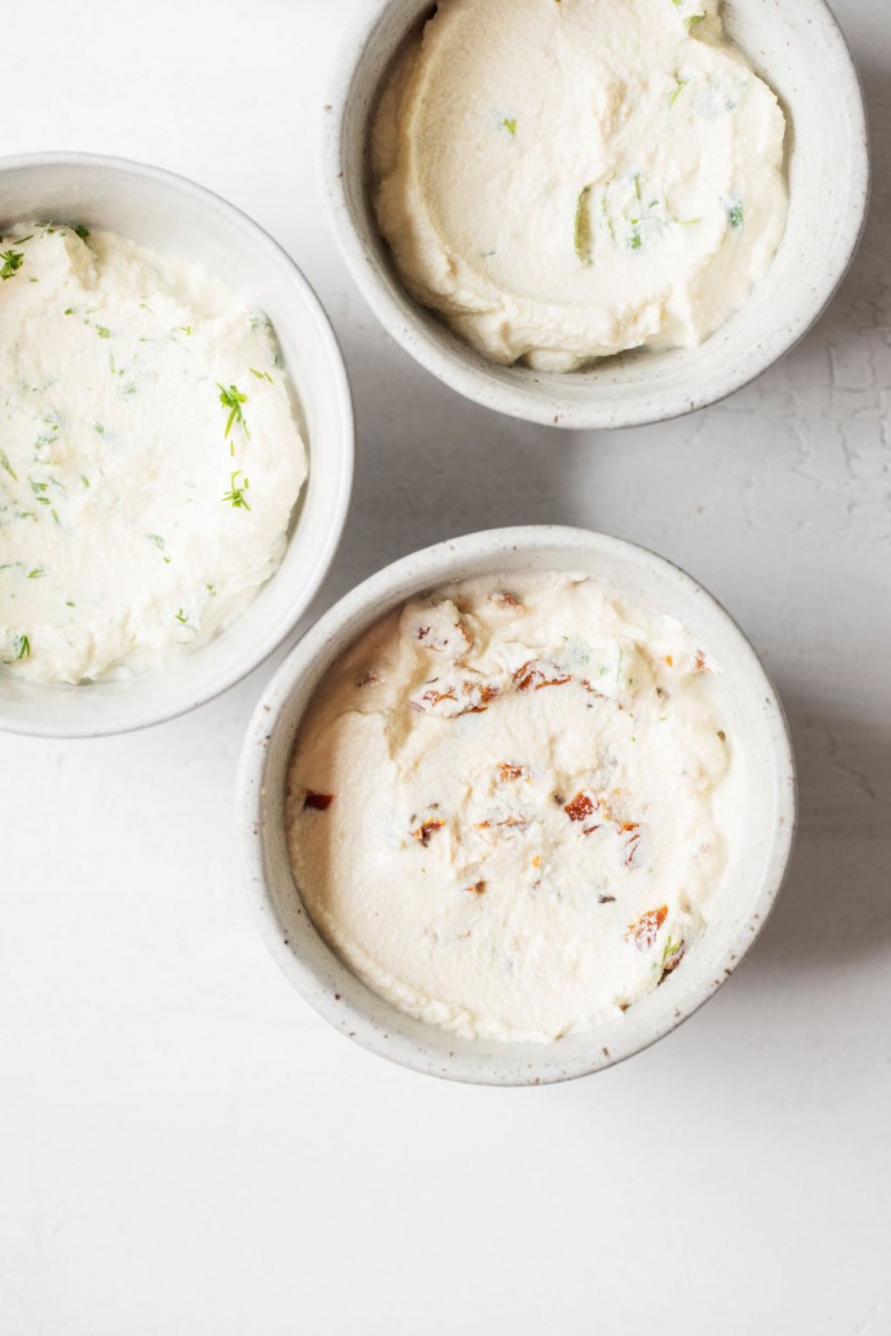 Three round, small ceramic bowls of a creamy, white dip rest against a white surface.