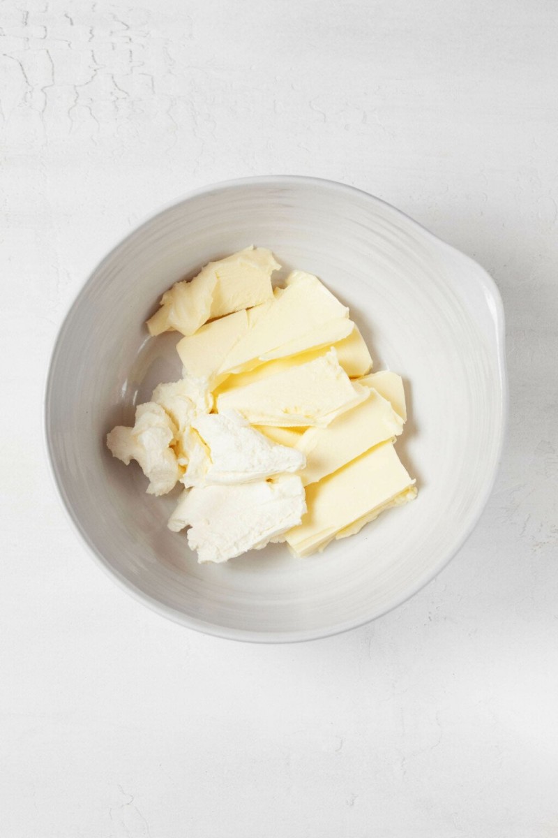 An overhead image of a white bowl, filled with butter and cream cheese. It rests on a white surface.