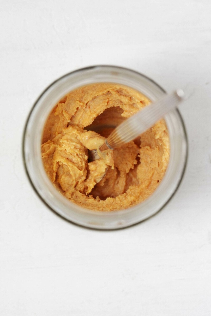 A very thick paste, which uses tahini as an ingredient, is in a jar. It's being mixed with a spoon.