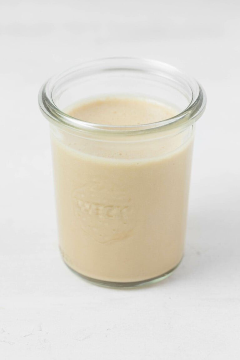 An image of a Weck mason jar, resting on a white surface, filled with a creamy miso sesame dressing.