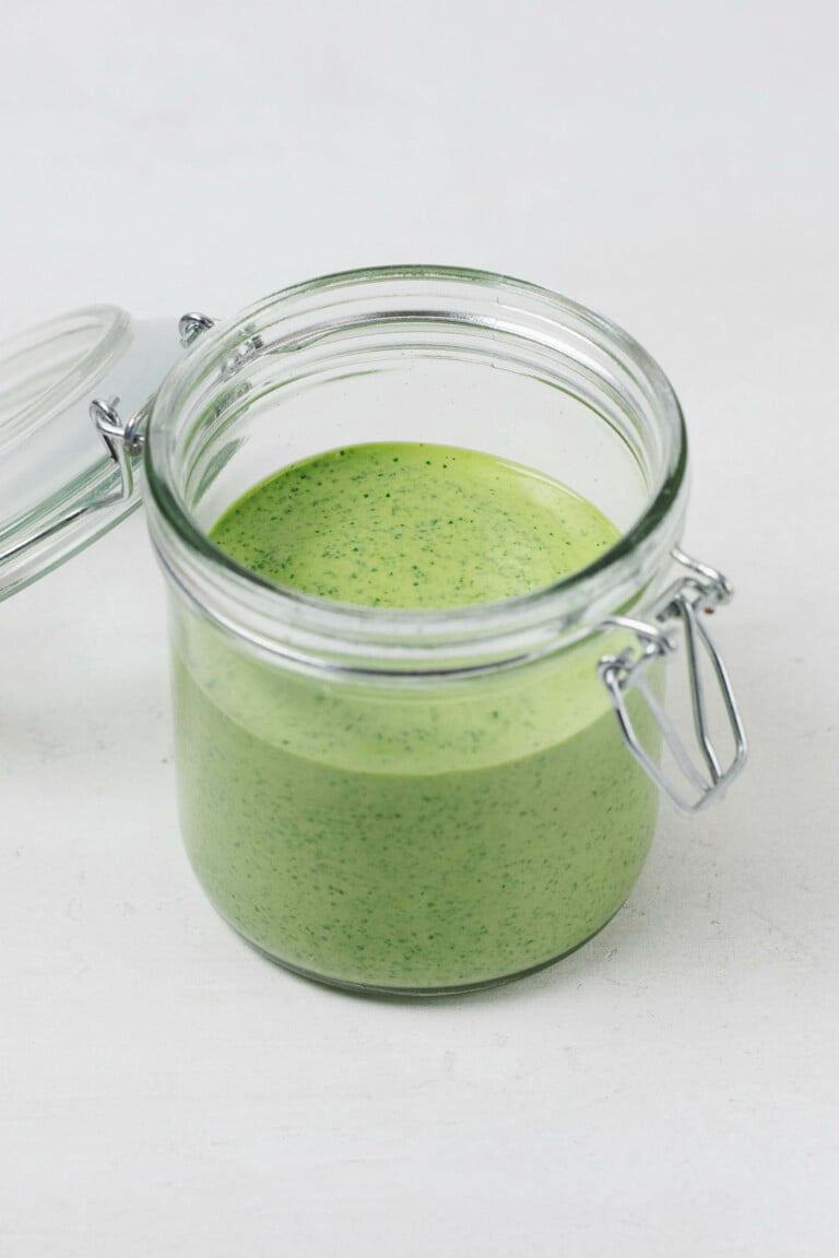 An image of a glass mason jar with a flip top lid, which holds a brighly colored green tahini dressing.